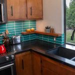 Close up of a kitchen with black Quartz counters, a black sink, and reddish, brown cabinets.